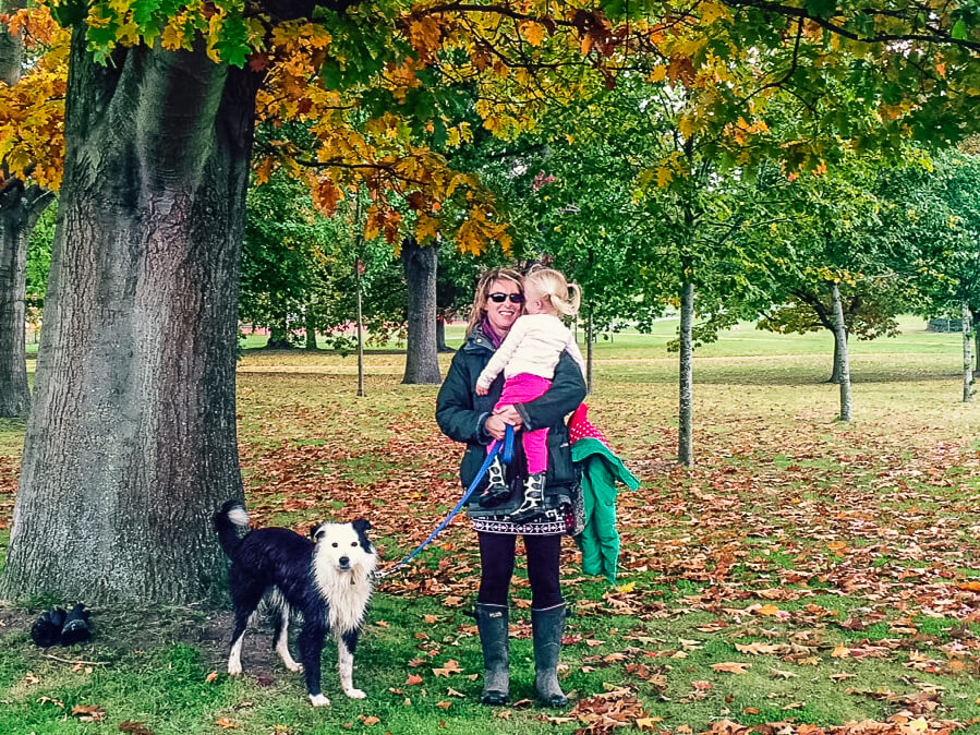 Woman holding young girl and dog in a park