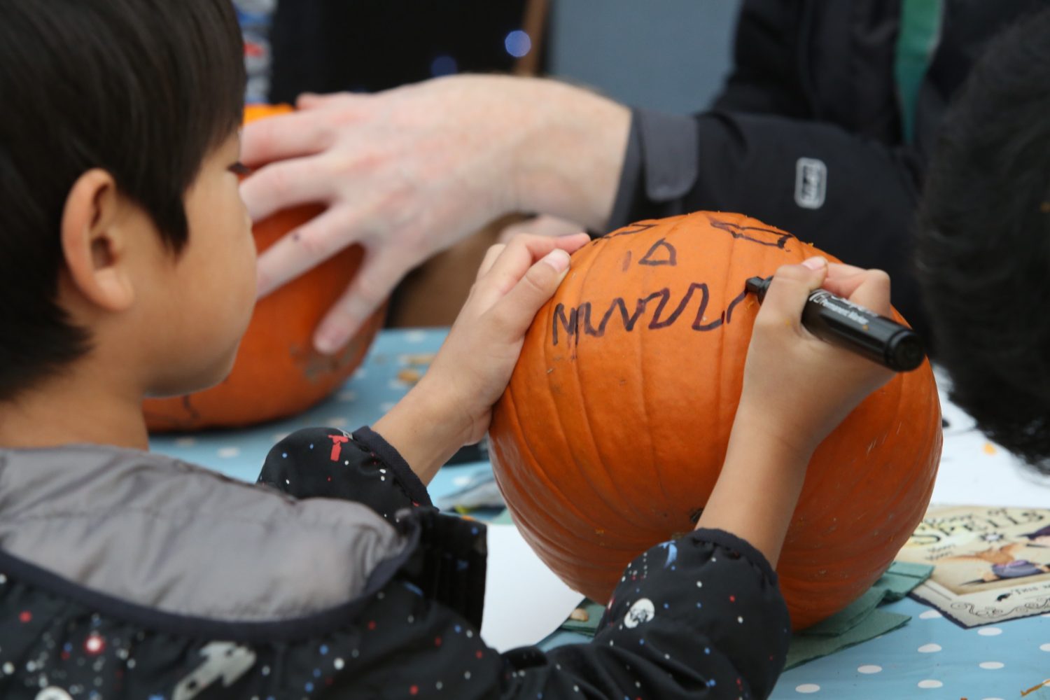 Young boy drawing a face on a pumpkin
