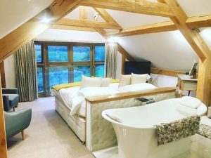 Large guest room with wooden beams and bath tub behind bed