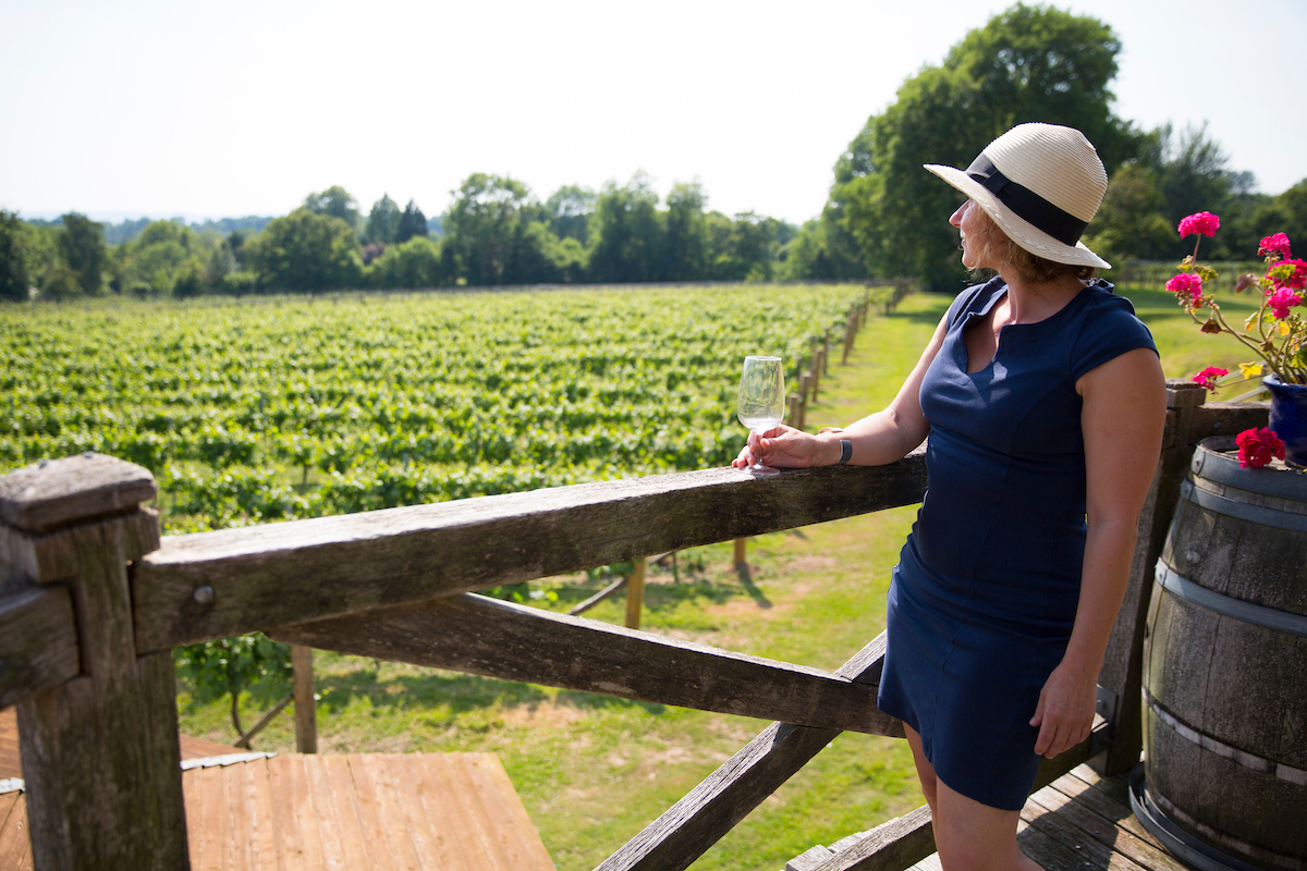 A woman in a hat looking out over the vineyard and tasting wine at Nutbourne Vineyard