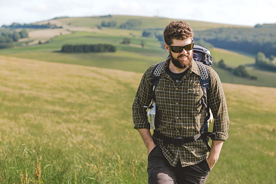 Man with beard, sunglasses and rucksack walking in the country