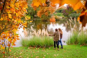 Two people standing by the lake at Wakehurst, framed by autumnal leaves