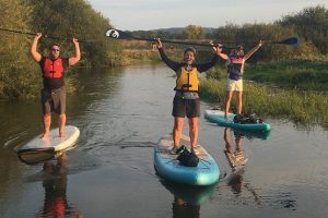 Three paddleboarders standing on their paddleboards holding the ore above their head