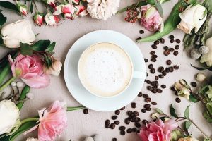a mug of frothy coffee surrounded by flowers and coffee beans
